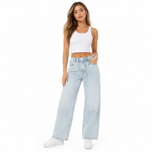 Load image into Gallery viewer, A woman modeling a pair of light-wash wide-leg denim jeans with a white crop tank top and white sneakers, standing against a plain white background.