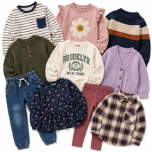 Load image into Gallery viewer, A flat lay of eight children's clothing items arranged together on a white background, including striped and solid long-sleeve tops, a sweater, jeans, leggings, a cardigan, a floral blouse, and a plaid shirt.
